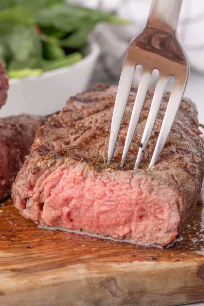 A fork is piercing the grilled sirloin steak.