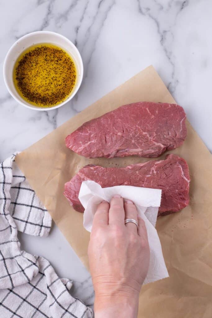 Two steaks being pat dry with a paper towel.