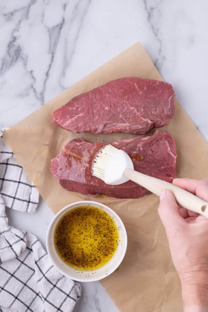 Steaks are brushed with with olive oil, salt, black pepper, and garlic powder mixture.