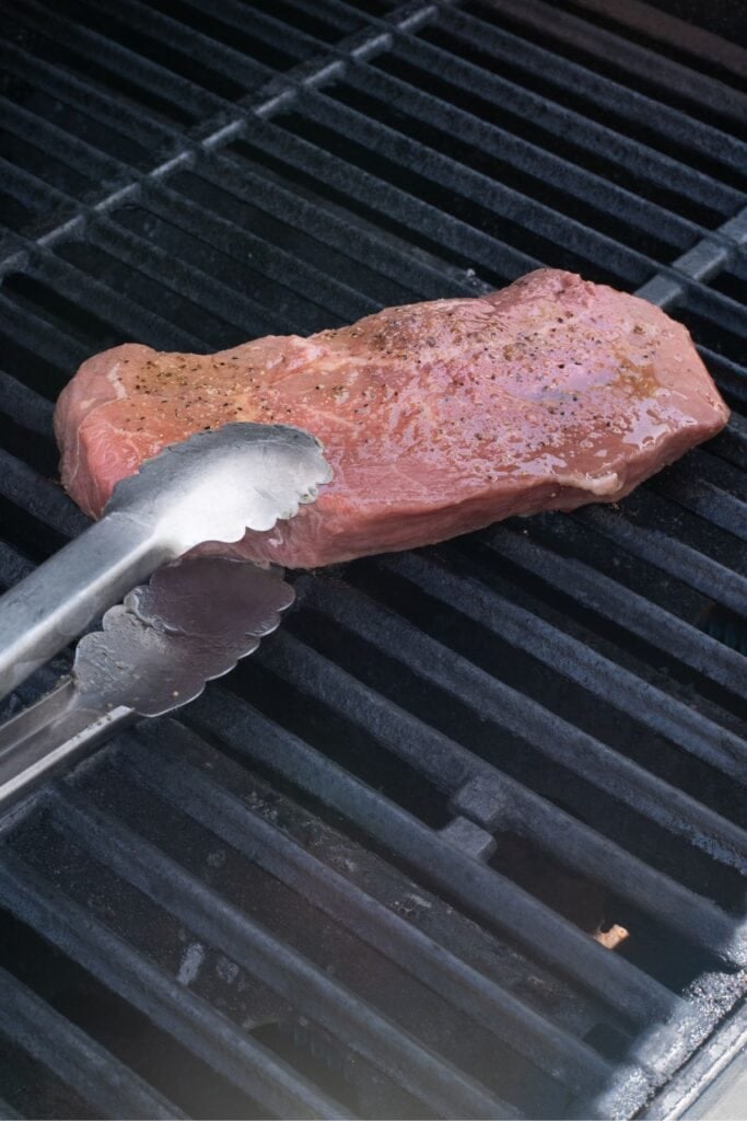 Raw steak placed on hot grill grates.
