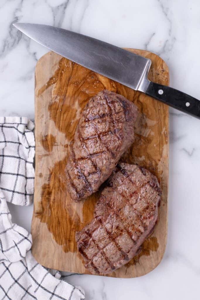 Two completed grilled steaks resting on a wood cutting board.