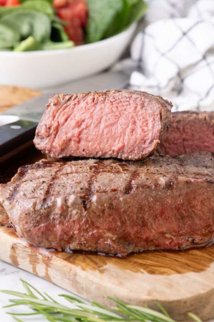 Two steaks stacked on top of each other. The top steak is sliced in half to show the interior.