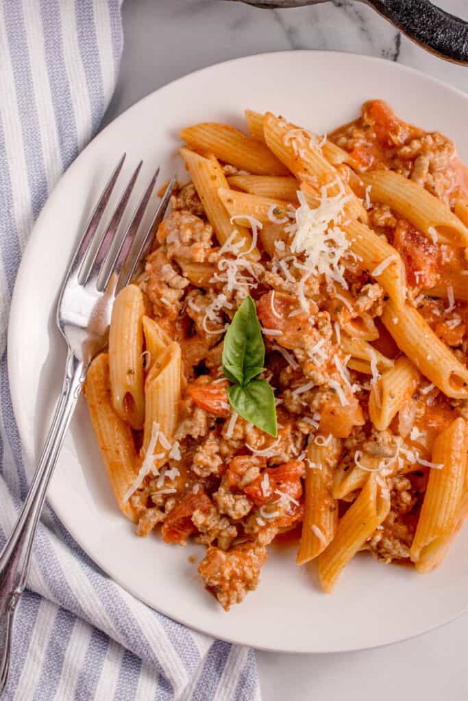 Completed ground turkey pasta served on a white dinner plate with a sprig of basil for garnish.