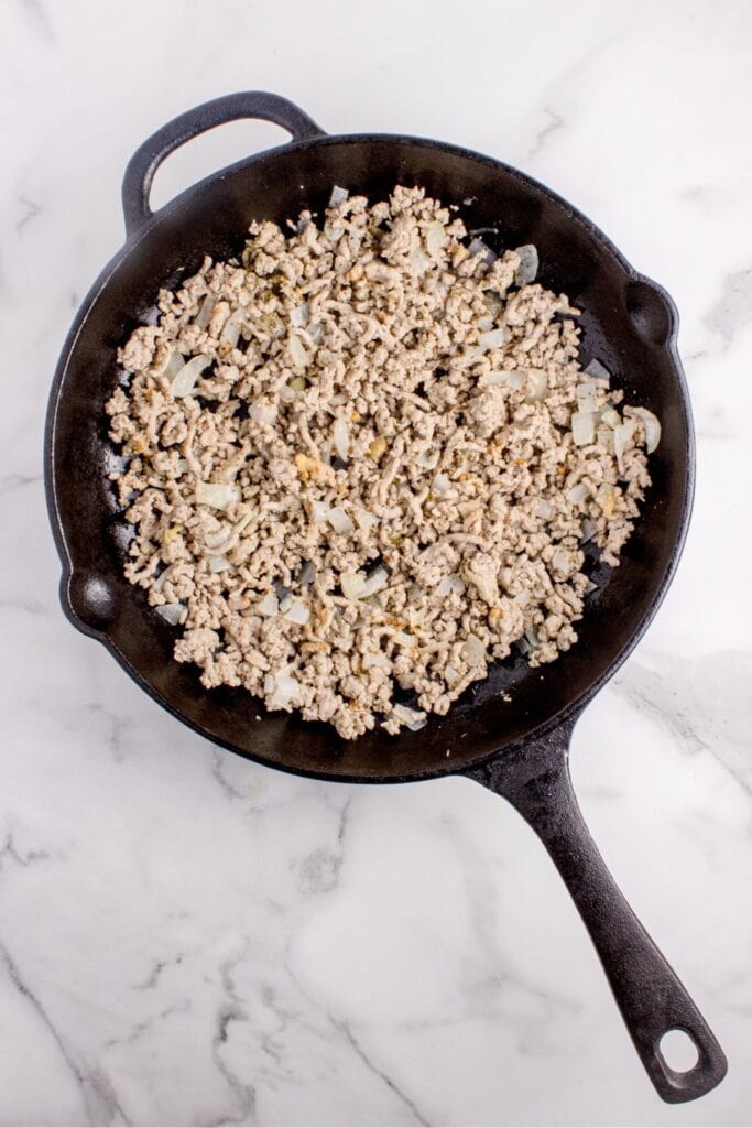 Ground turkey, chopped onions, and spices cooking in a cast iron pan.