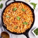 Ground turkey pasta in a black cast iron pan garnished with grated parmesan and basil leaves.
