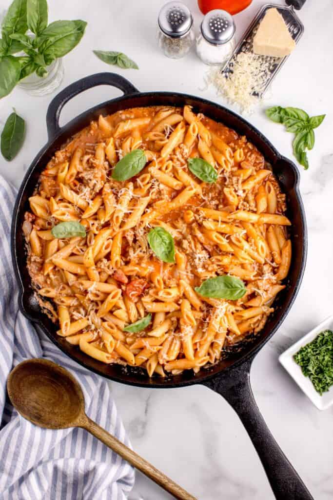 Ground turkey pasta in a black cast iron pan garnished with grated parmesan and basil leaves.