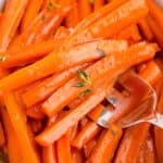 Maple glazed carrots in a white serving dish. A serving fork is holding a serving of carrots.