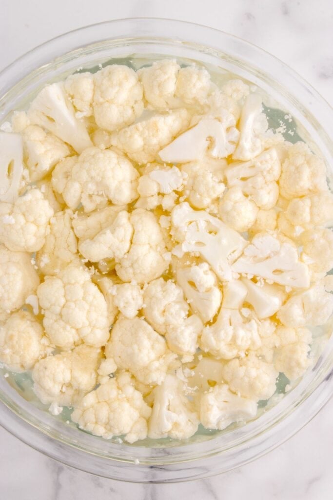 Cauliflower being cleaned in a glass bowl with water.