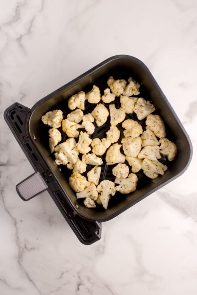 Uncooked cauliflower arranged in an air fryer basket.