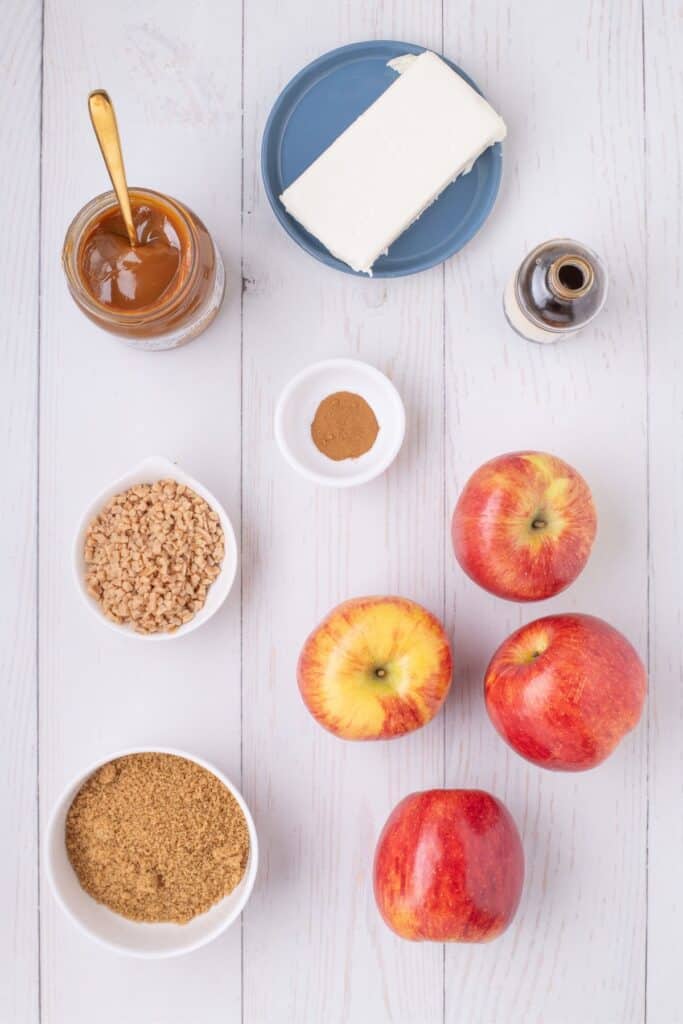 Ingredients for caramel apple dip: cream cheese, brown sugar, vanilla extract, ground cinnamon, caramel, toffee bits, and apples.