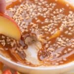 An apple is scooping up a bite of caramel dip.