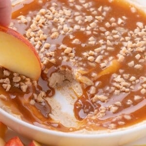 An apple is scooping up a bite of caramel dip.