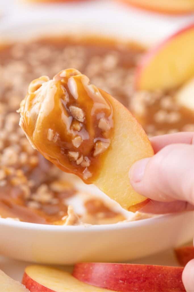 A hand is holding up an apple slice with caramel dip on it.