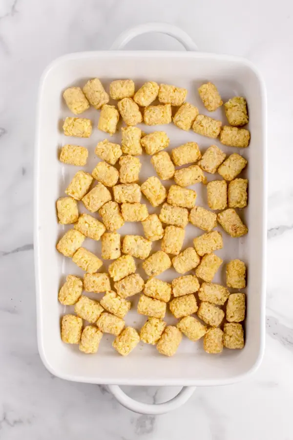Layers of chicken tater tot casserole being layered in a baking dish.