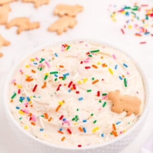 Completed Funfetti dip in a white bowl. Dip is decorated with rainbow sprinkles and a single animal cracker.
