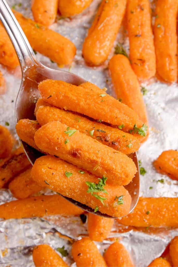 A serving spoon lifting up a serving of cooked baby carrots.
