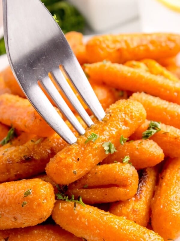 A fork is piercing a roasted baby carrot.