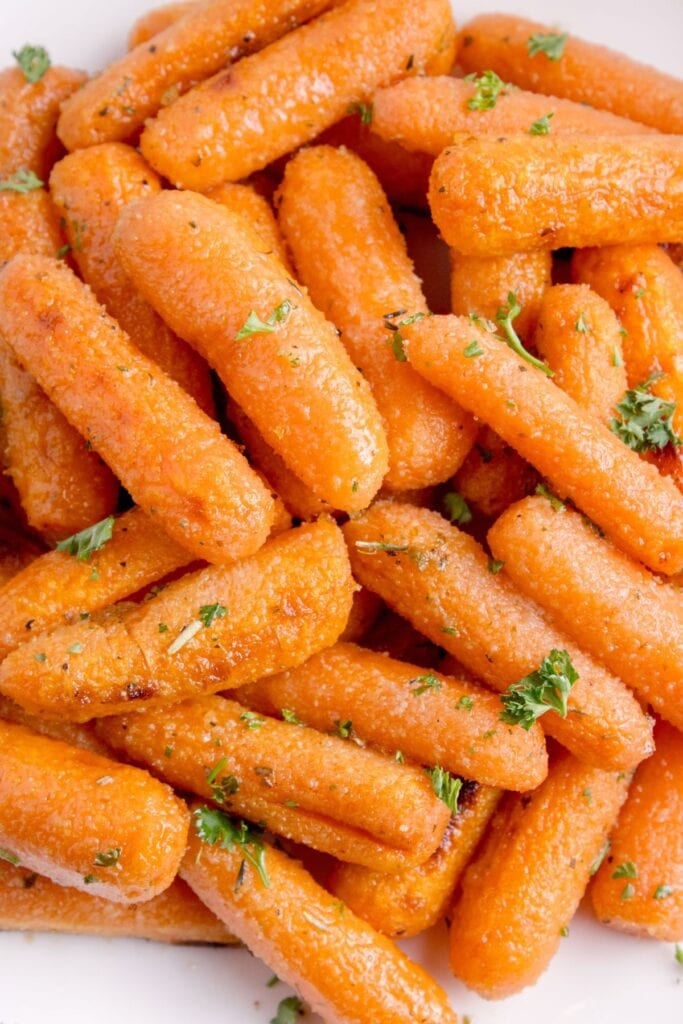 Roasted carrots on a white dinner plate garnished with fresh parsley.