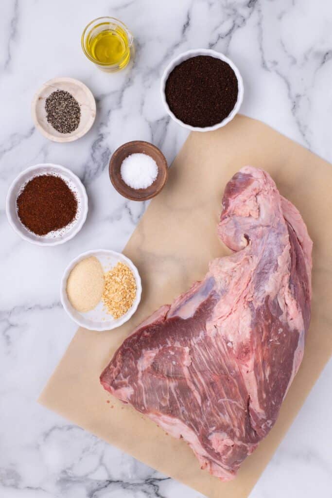 Ingredients for tri tip in the oven: ground coffee, chili powder, salt, black pepper, onion powder, garlic powder, whole tri-tip, and avocado oil.
