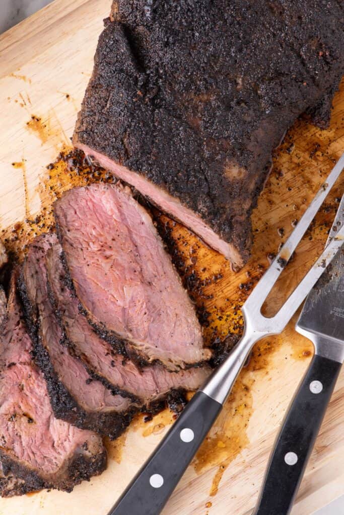 Large tri tip partially sliced and fanned out on a wooden cutting board.