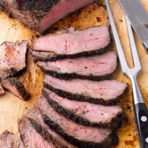 Large tri tip partially sliced and fanned out on a wooden cutting board.