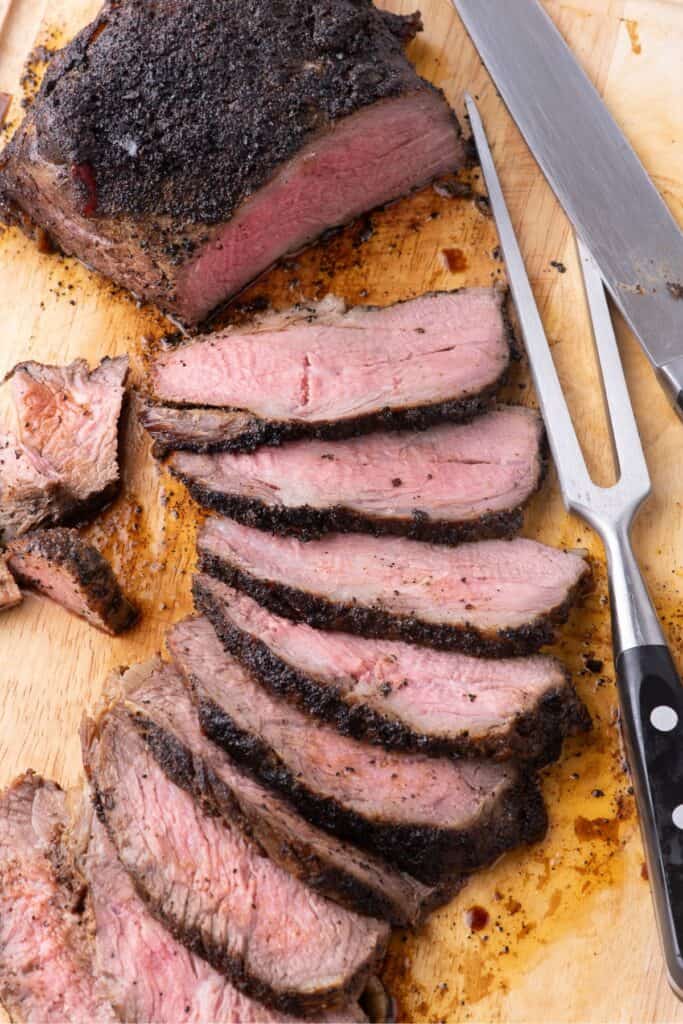 Large tri tip partially sliced and fanned out on a wooden cutting board.