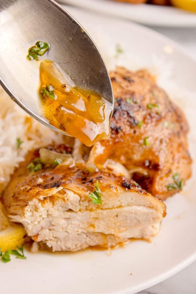 Cooked chicken thighs with a spoon drizzling an onion gravy on top.