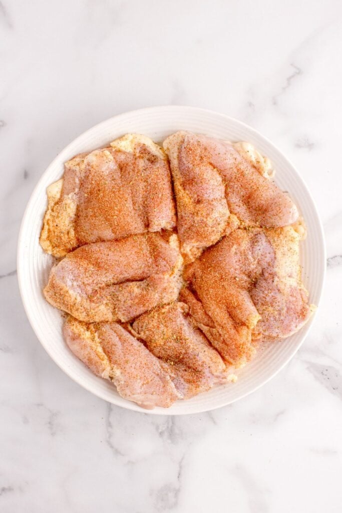 Chicken thighs seasoned on a white plate.