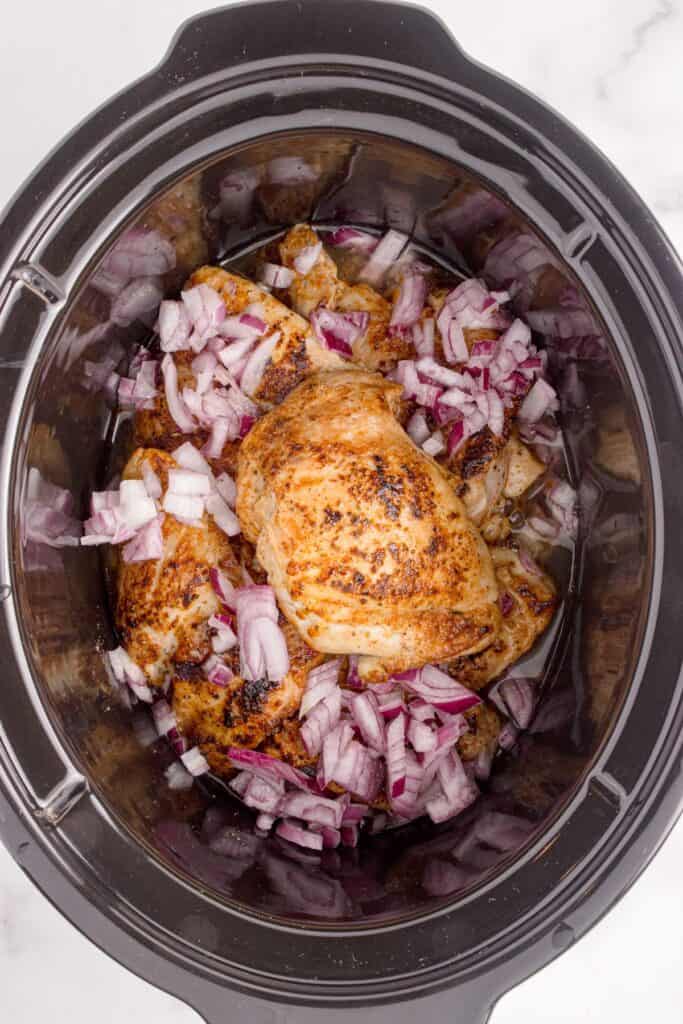 Chopped red onion added to the crock pot insert with cooked chicken thighs.