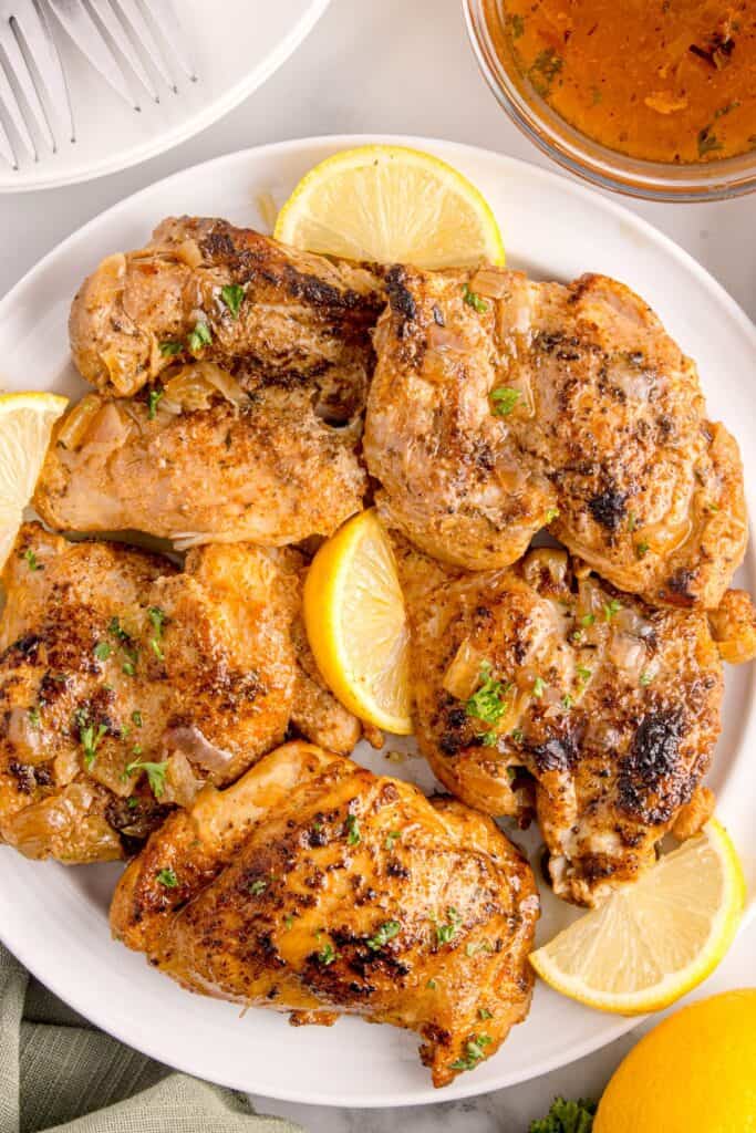 Cooked chicken thighs on a white serving platter with lemon wedges as garnish.