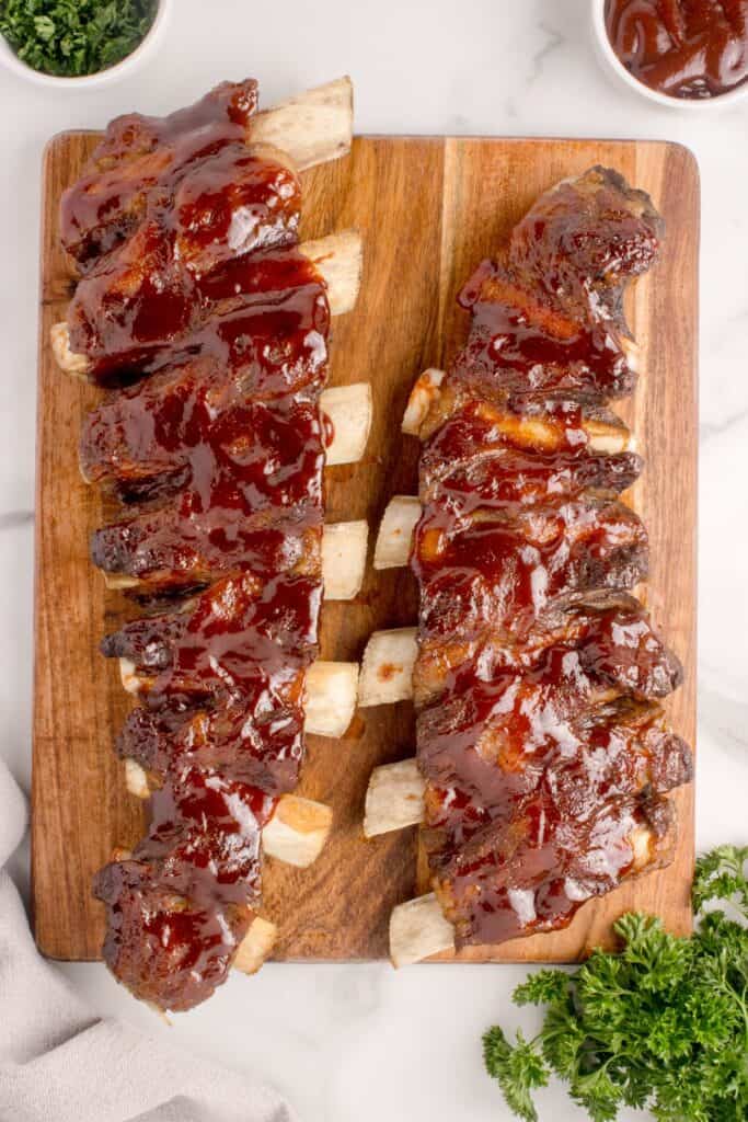 Two racks of finished beef ribs on a wooden cutting board.