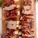 Two racks of beef ribs sliced and sauced on a wooden cutting board.