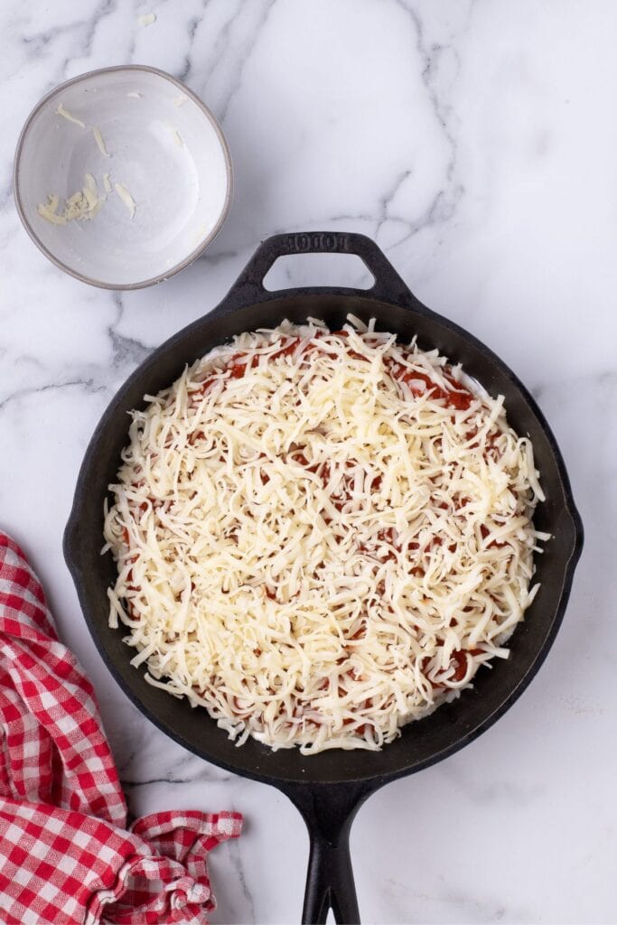 Remaining mozzarella is sprinkled on top of the pizza sauce.