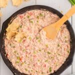 Completed sausage cream cheese dip in cast iron pan with a wooden spatula.