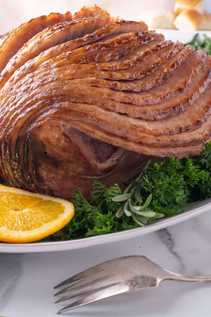 Completed glazed spiral ham on a white serving platter. The slices of ham are leaning to show detail.