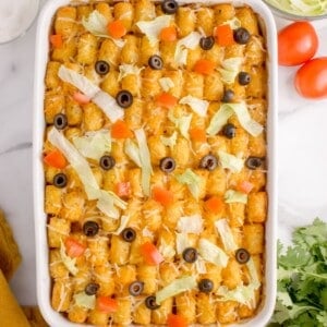 Finished taco tater tot casserole in a white baking dish with lettuce, sliced black olives, and diced tomatoes on top.