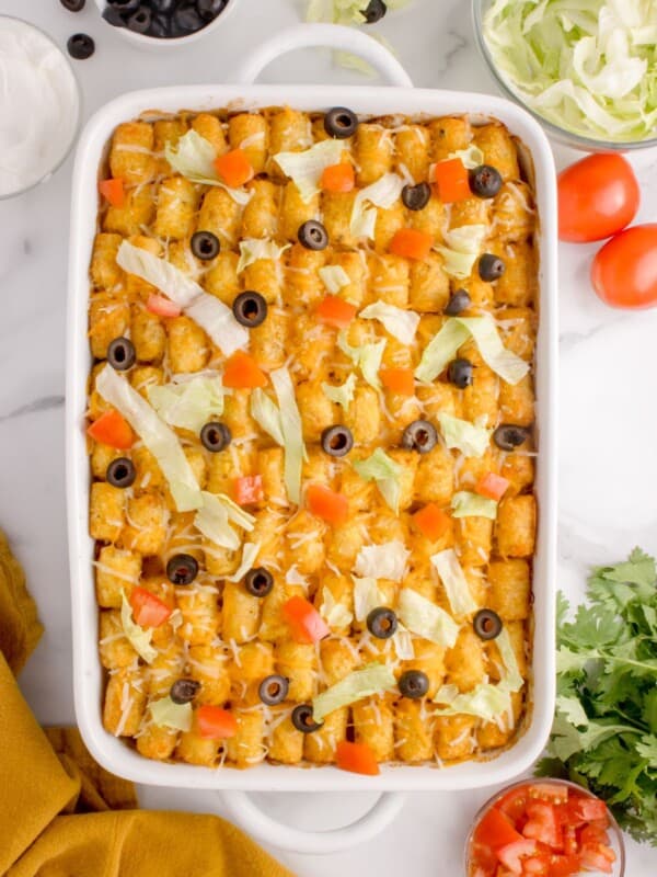 Finished taco tater tot casserole in a white baking dish with lettuce, sliced black olives, and diced tomatoes on top.