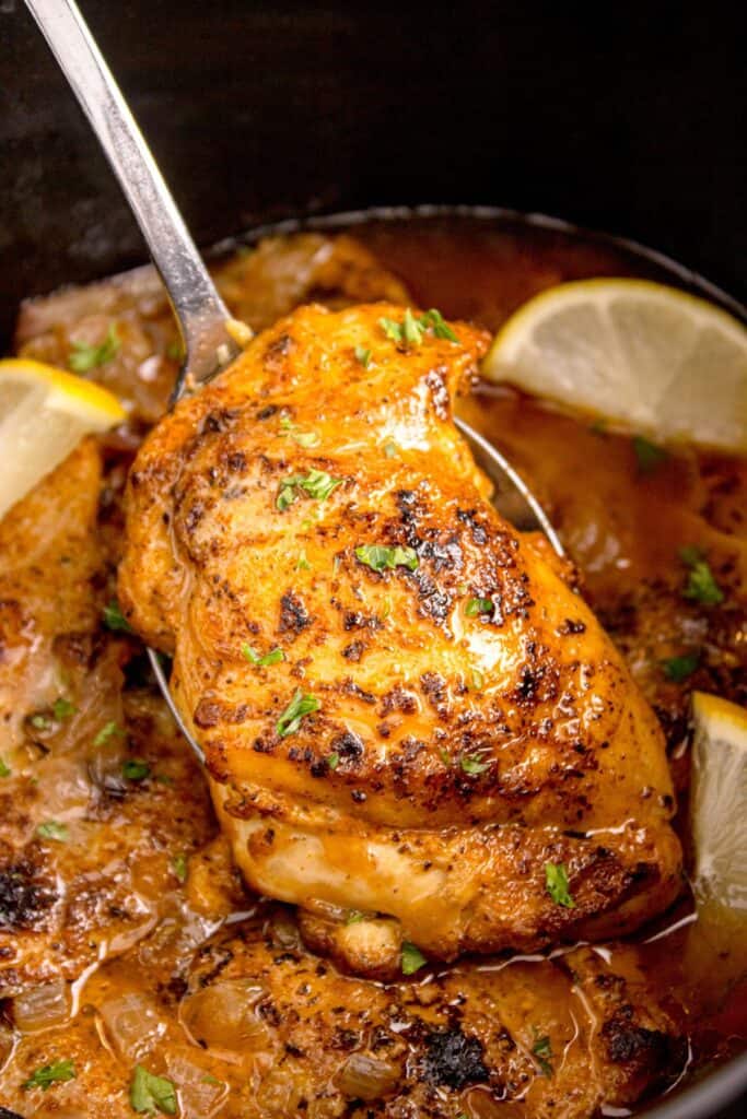 Cooked chicken thighs being lifted from the slow cooker.