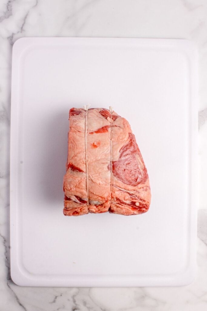 Raw prime rib cut tied with twine on a white cutting board.
