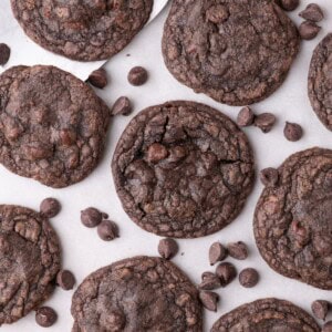 Completed fudge cookies on a parchment lined baking sheet. Chocolate chips are scattered across the baking tray.