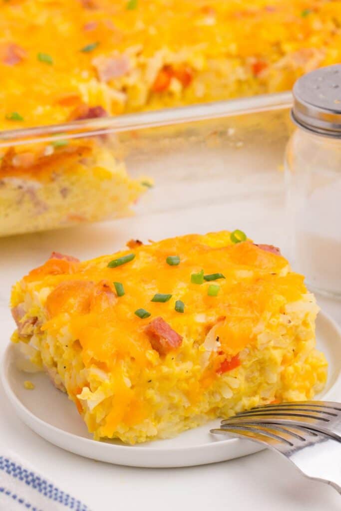 A serving of ham and egg casserole on a small white plate with two forks resting on the edge.