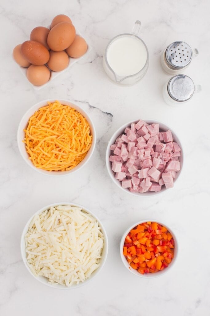 Ingredients for Ham and Egg Casserole: Eggs, milk, cheddar cheese, ham, hash browns, bell pepper, salt, and pepper.