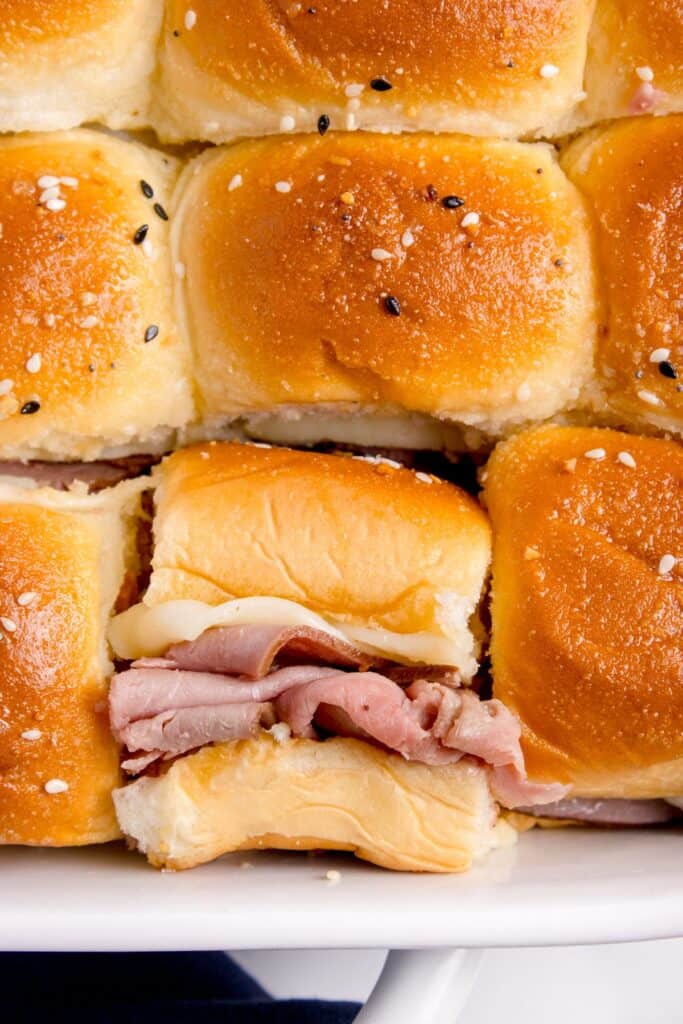 Baking pan with completed roast beef sliders. One has been cut out and turned to the side to show the cross section.