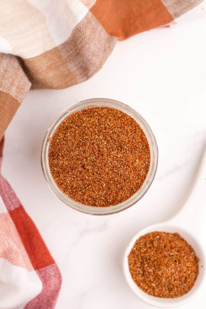 Chili seasoning in a short mason jar. A tablespoon is next to the jar with a scoop of seasoning in it.