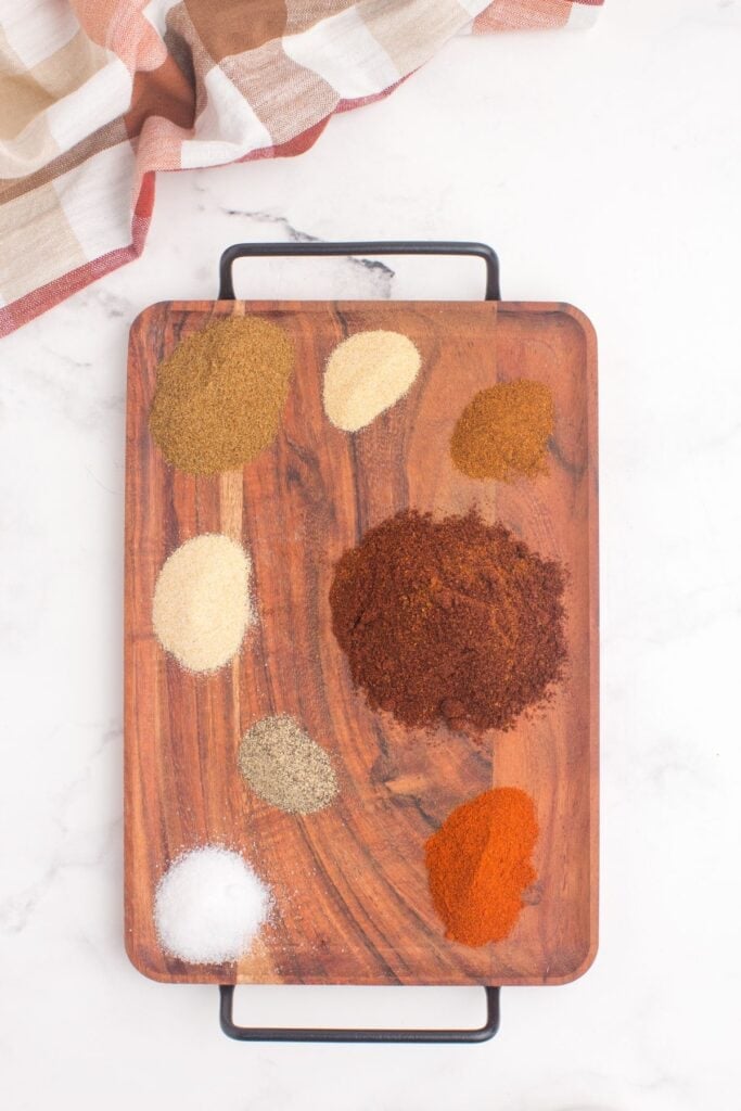 Wooden serving platter with several mounds of seasonings on it.
