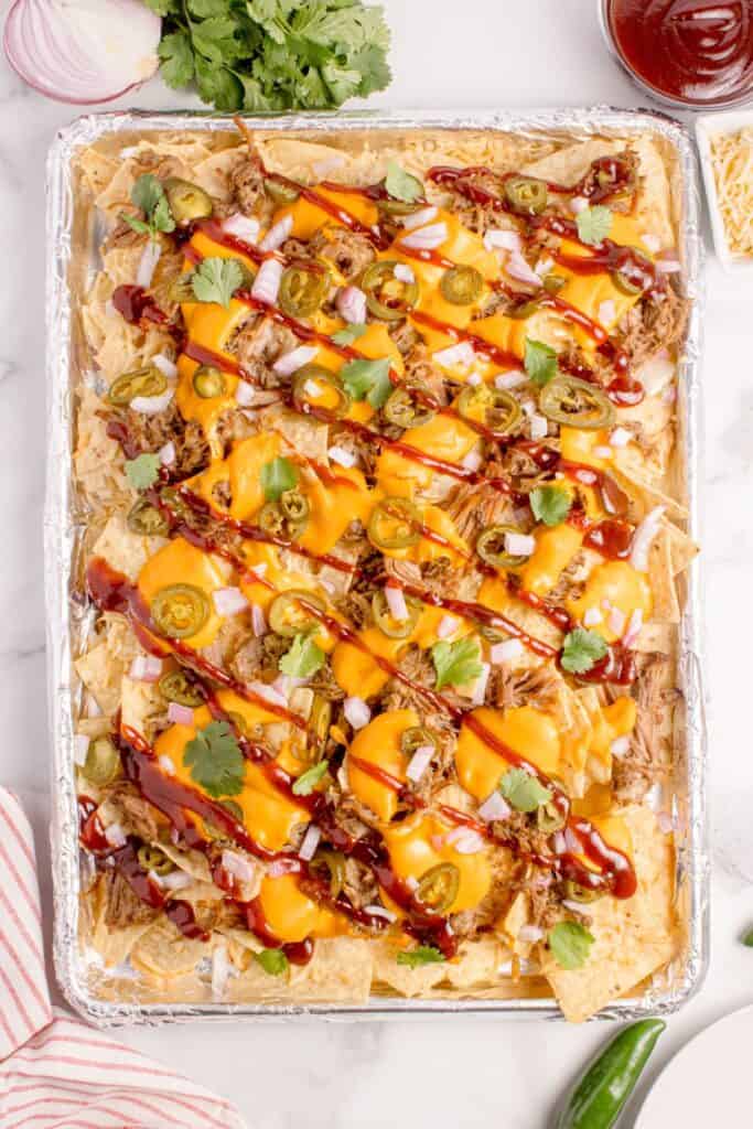 Pulled pork nachos on a aluminum foil covered baking sheet.
