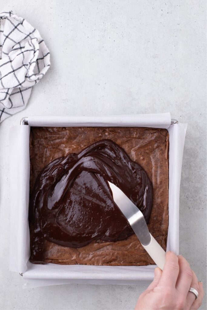 Baked brownies are frosted with a chocolate ganache.