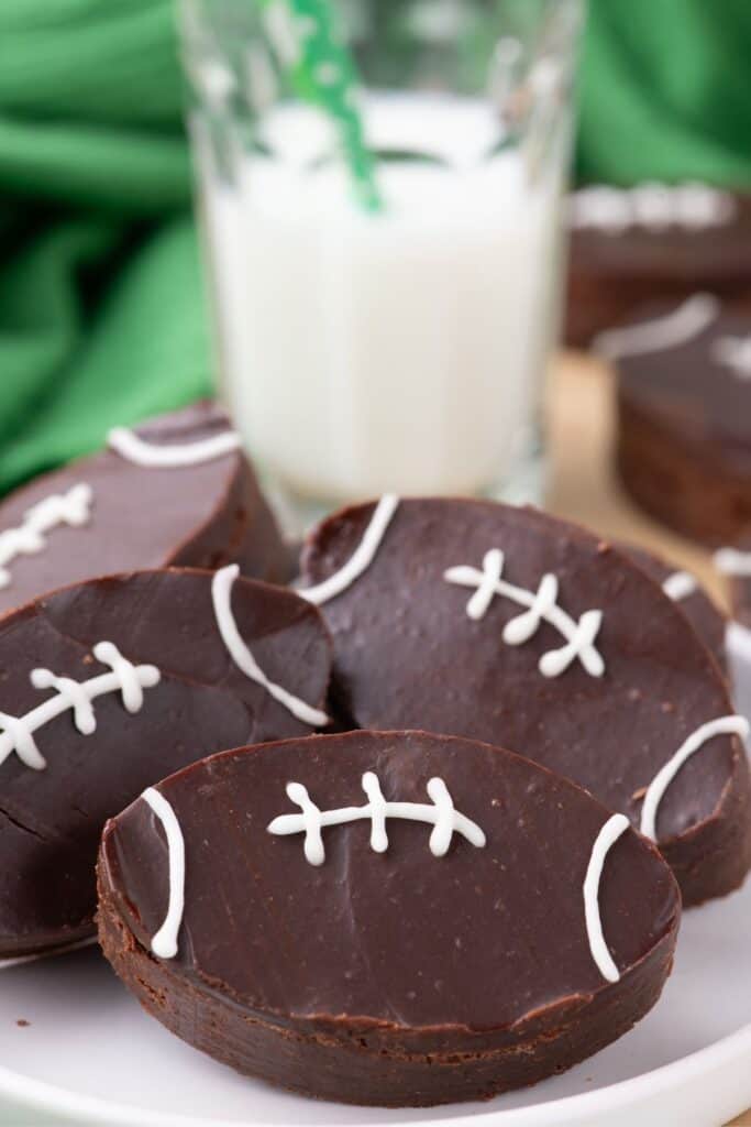 Football brownies fanned out on a white plate. A glass of milk is behind the plate.