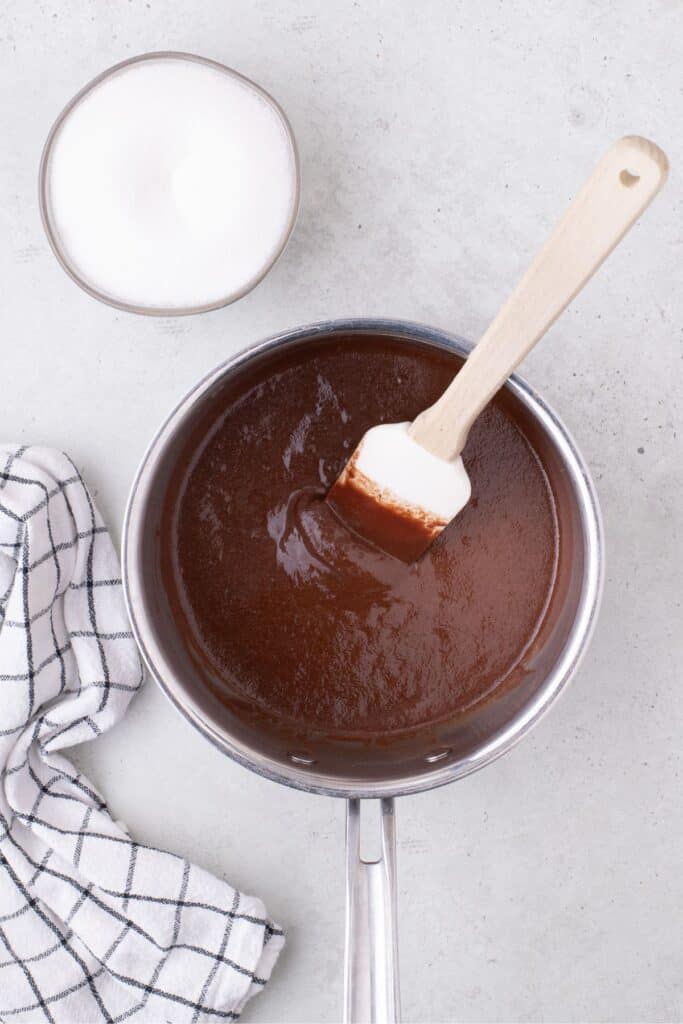 Saucepan with chocolate chips and butter melted together. A bowl of sugar is next to the saucepan.