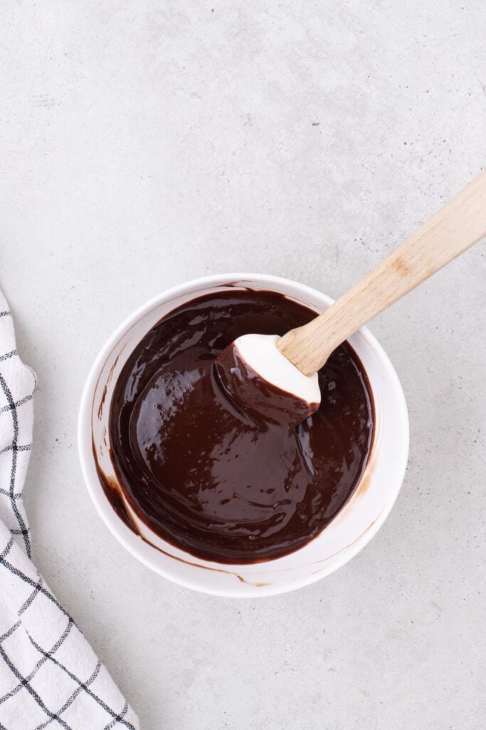 heavy cream and melted chocolate chips are combined in a small white bowl to make a ganache.